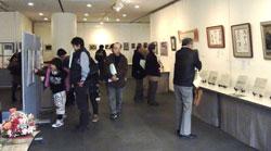 美術展に並ぶ絵を人々が見ている写真