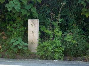 道端の草の茂みの中に立つ「小白水」と文字が彫られた白い石柱の写真