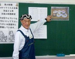 藍色のエプロンをつけた男性が黒板の前で説明している写真