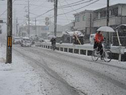 雪が積もっている中を自転車で走っている人の写真