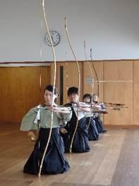 袴姿の4人の人が、弓を持ちひざをつき一列に並んでいる写真