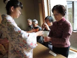 着物姿の女性が、参加者にお茶をふるまっている様子の写真