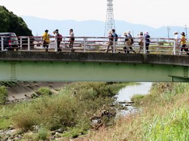 緑の古い橋を2列で人が渡っており、背景には、山が連なっている写真