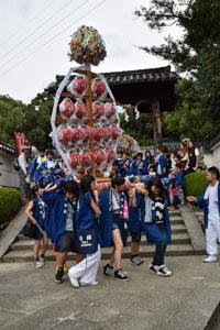 小泉神社の境内にある石造りの階段の前で、青い法被を着た子どもたちが赤い提灯がいくつもついた神輿を担いでいる様子の写真