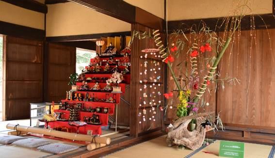 和室の中に大きなひな壇と、竹と野の花と和風の小物を使ったモニュメントが鎮座している写真