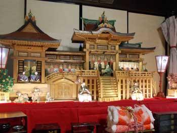 ひな壇に立派な神殿が丸々乗せられ、昔の生活様式を象った場所に配置されているひな飾りの写真