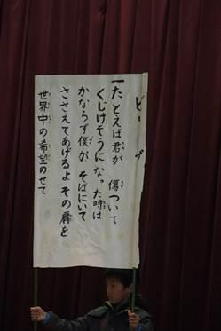 ビリーブという歌の歌詞が書かれた模造紙を掲げている小学生の写真