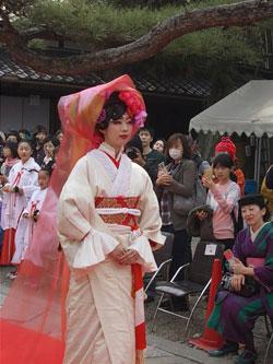 白い着物に赤いベールをまとった女性が歩く写真