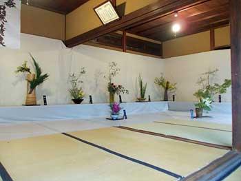 畳と土壁の和室に飾られた8つの生け花作品の写真