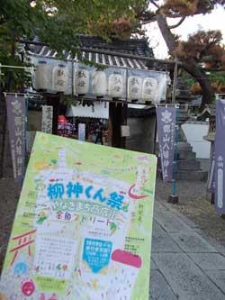 お社と祭提灯を背景に映る柳神くん祭のポスターの写真
