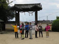 小泉神社の門を背景に、ガイドの案内を聞く参加者たちの写真