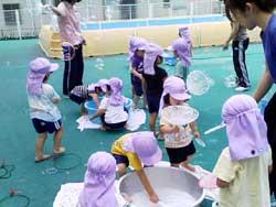 藤色の帽子を被って、シャボン玉遊びをしている保育園児たちの写真
