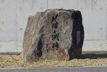 コンクリートの擁壁の前の芝生の上に立つ「八条ケ渕跡」と彫られた四角い石碑の写真