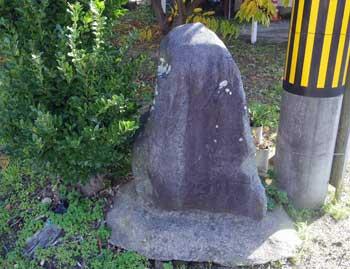道ばたの電信柱の根元の脇に佇む目立たない小さな石碑の写真