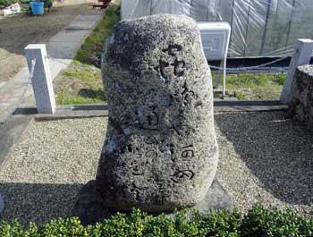 白い石柱と鎖で囲まれた敷地内に立つ石造りの句碑の写真