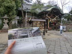 左下に案内ちらしを持った人の手が映り込んでいる、神社へと続く石畳の道から緑色の瓦屋根の神社を見ている視点の写真