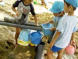 青い帽子を被り、樋から水を流して遊ぶ保育園児の男の子たちの写真