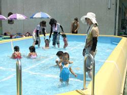 子ども用プールで遊ぶ青い水着を着た子どもの写真