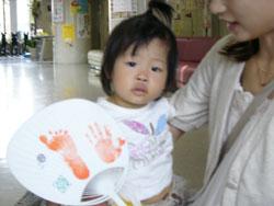 手形と足形が押されたうちわを手に撮影した女児と保護者の写真