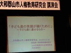 講演会の看板の下に設置されたモニターにタイトルが写っている写真