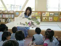 絵本の読み聞かせをしている西村千鶴子さんと静かに聞き入っている園児たちの写真