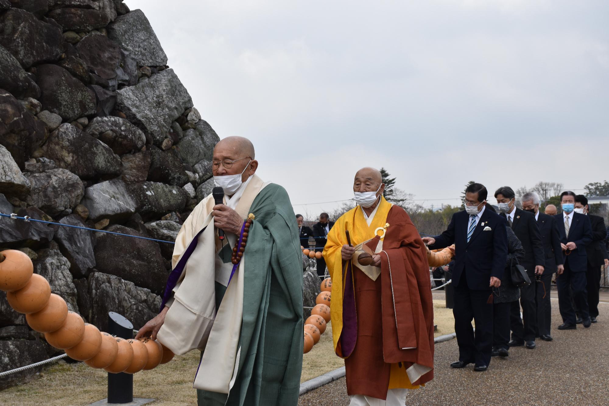 僧侶2人の先導で天守台の周りの数珠をくる参列者