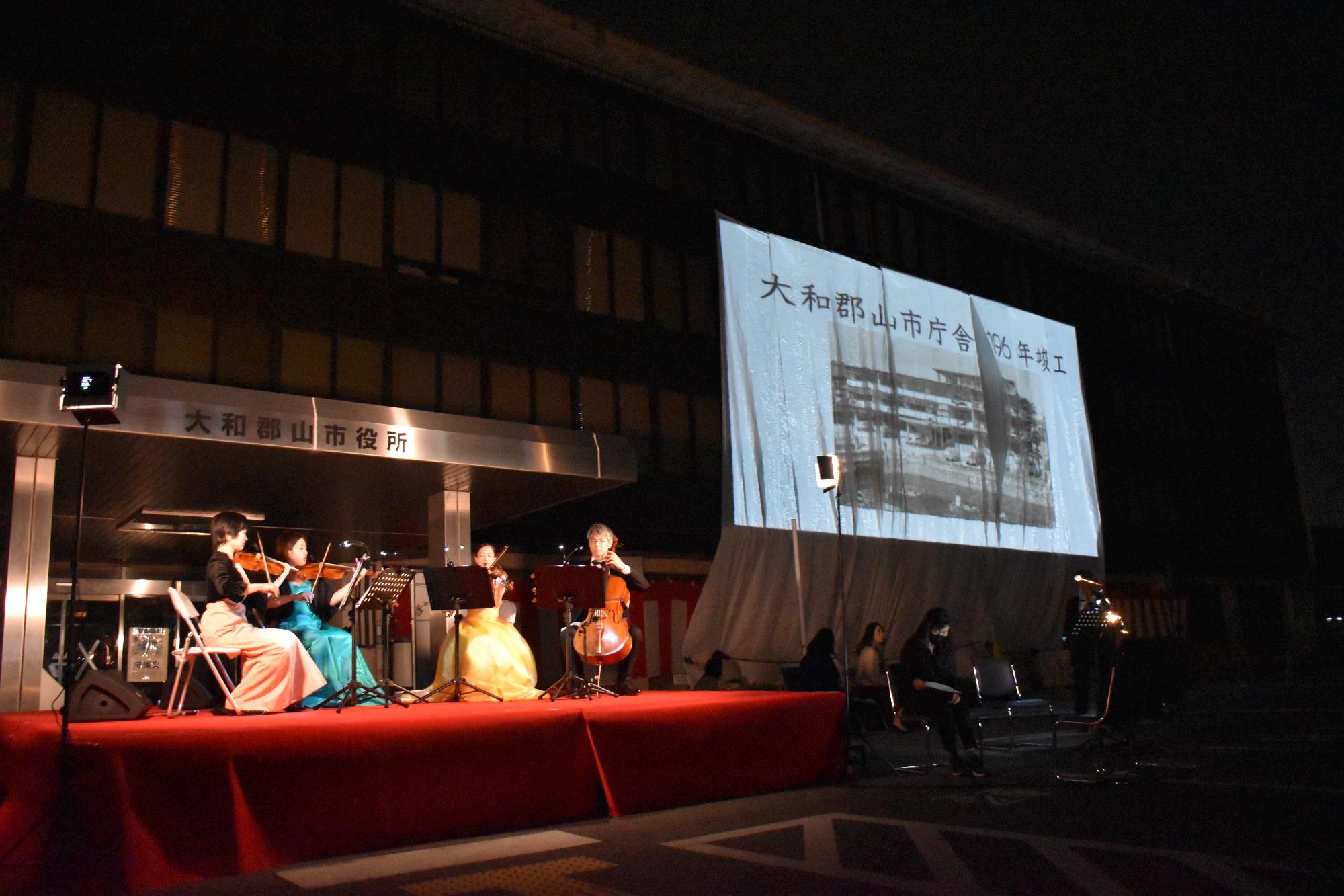 弦楽器を演奏する4人の奏者と旧庁舎に貼られたスクリーンに映し出される映像