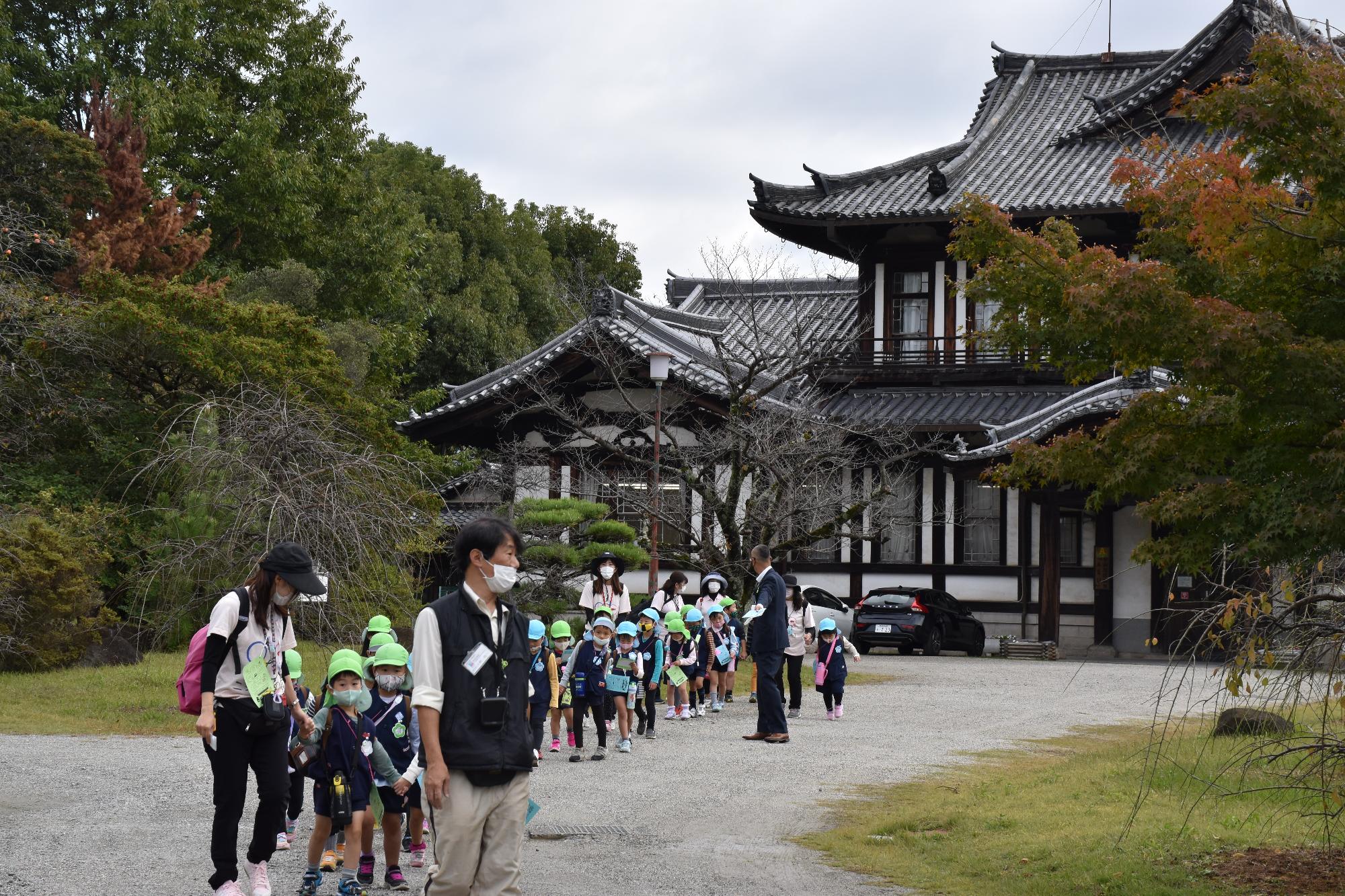 瓦葺の城址会館の前から出発し歩く幼稚園児の列