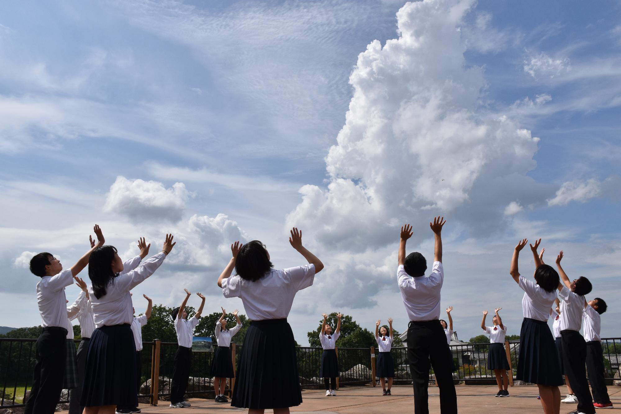 円に並び、空に向かって手を振る制服を着た中学生達