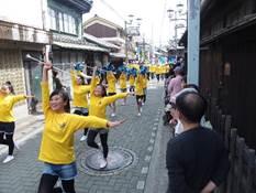 黄色いシャツを着た女性の一団が踊りながらパレードしている処の写真