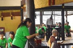 緑色のTシャツを着た女性たちが立っていて、その前に僧侶が座っている写真