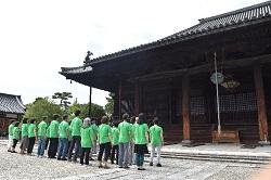 緑色のTシャツを着た男女がお寺の入り口の前に並んでいる写真
