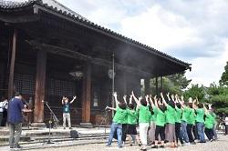 緑色のTシャツを着た多くの男女が両手を上に広げている後ろ姿の写真