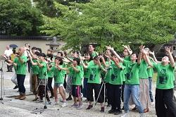 緑色のTシャツを着た多くの男女が上に向かって手を広げている様子の写真