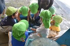 黄緑色の帽子を被った幼稚園児たちが屈んで作業している写真