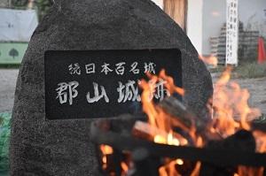 日本百名城郡山城跡と彫られている石碑とその前に置かれたかがり火の写真