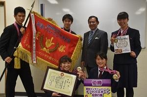市長と優勝旗を拡げて持つ男性2人と賞状とメダルをを持つ3人の男女の写真