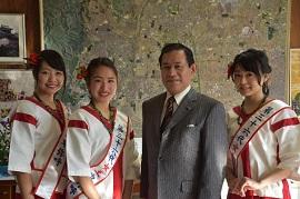 壁の前に並んでいる市長と、赤と白の衣装を着てたすきをかけた3人の女性の写真