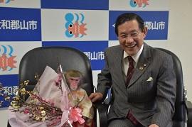 椅子に腰かけ、市長から送られた花束を持った芸猿の写真