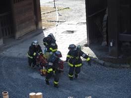 木製の門の前で赤い小型消防ポンプを移動させている消防服を着た4人の人物の写真