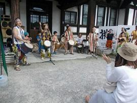 城址会館前にて、4人組の男性がラテン風の衣装を着て、太鼓で演奏している様子の写真