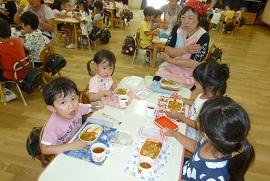 大きい子と小さい子が一緒になった4人の班でカレーライスを食べる子どもたちと女性の写真