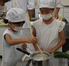 雪平鍋で茹でている様子を菜箸で確認している女子小学生2人の写真