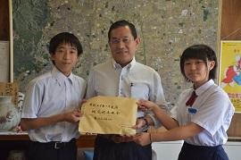 男女の中学生たちが集めた義援金を市長に手渡ししている様子の写真
