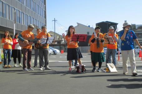 オレンジ色の揃いのウェアを着てビルの前に立つ人々の写真