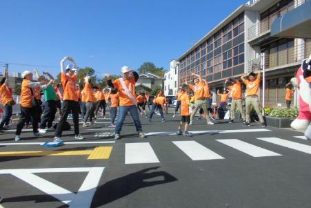 青空の下、横断歩道でオレンジ色の揃いのウェアを着た人々が立っている写真
