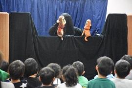 黒子が猿の人形を使って劇を演じているのを見つめている幼稚園児たちの写真