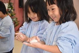お餅を丸めている幼稚園児の2人の女の子が微笑んでいる写真
