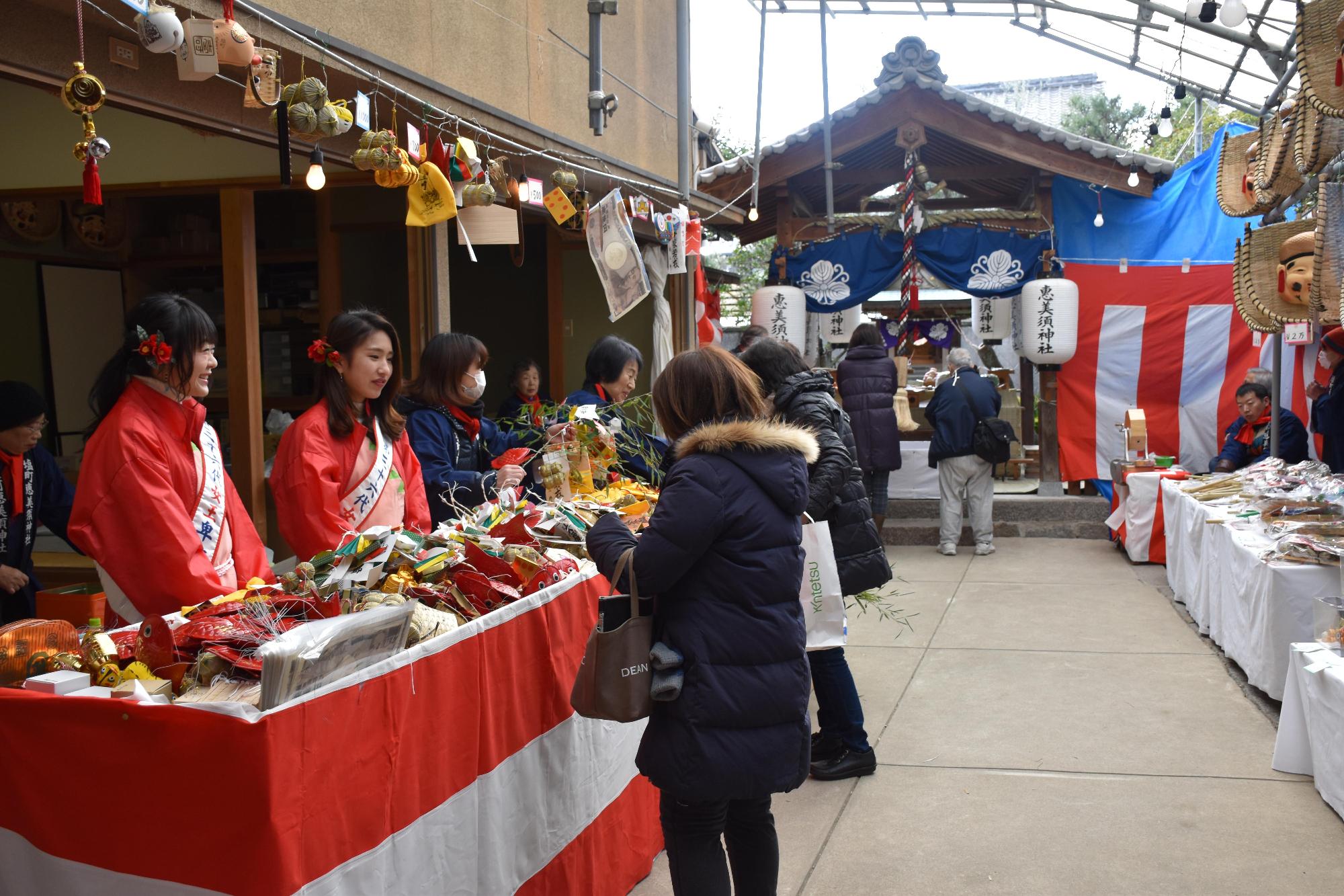 塩町恵美須神社の境内で赤い服着た女性たちがお守り販売している様子の写真