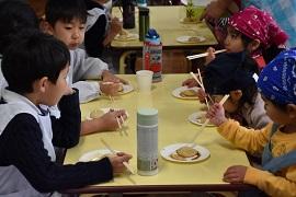 小学生と園児6人が仲良くきな粉餅を食べている様子の写真